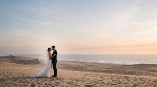 Wide editorial photograph of a wedding couple standing small within a vast, clean negative space, embodying minimalist composition with maximum emotional impact